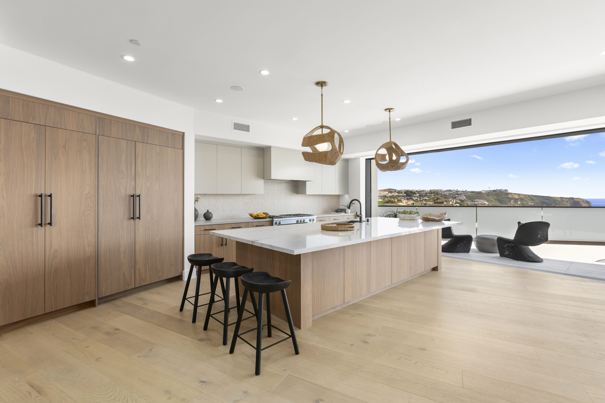 The chef’s kitchen is anchored by a large central island and appointed with a premium appliances, custom cabinetry, and a curated mix of quartz and quartzite countertops. Expansive sliding glass door leads seamlessly to outdoor deck.