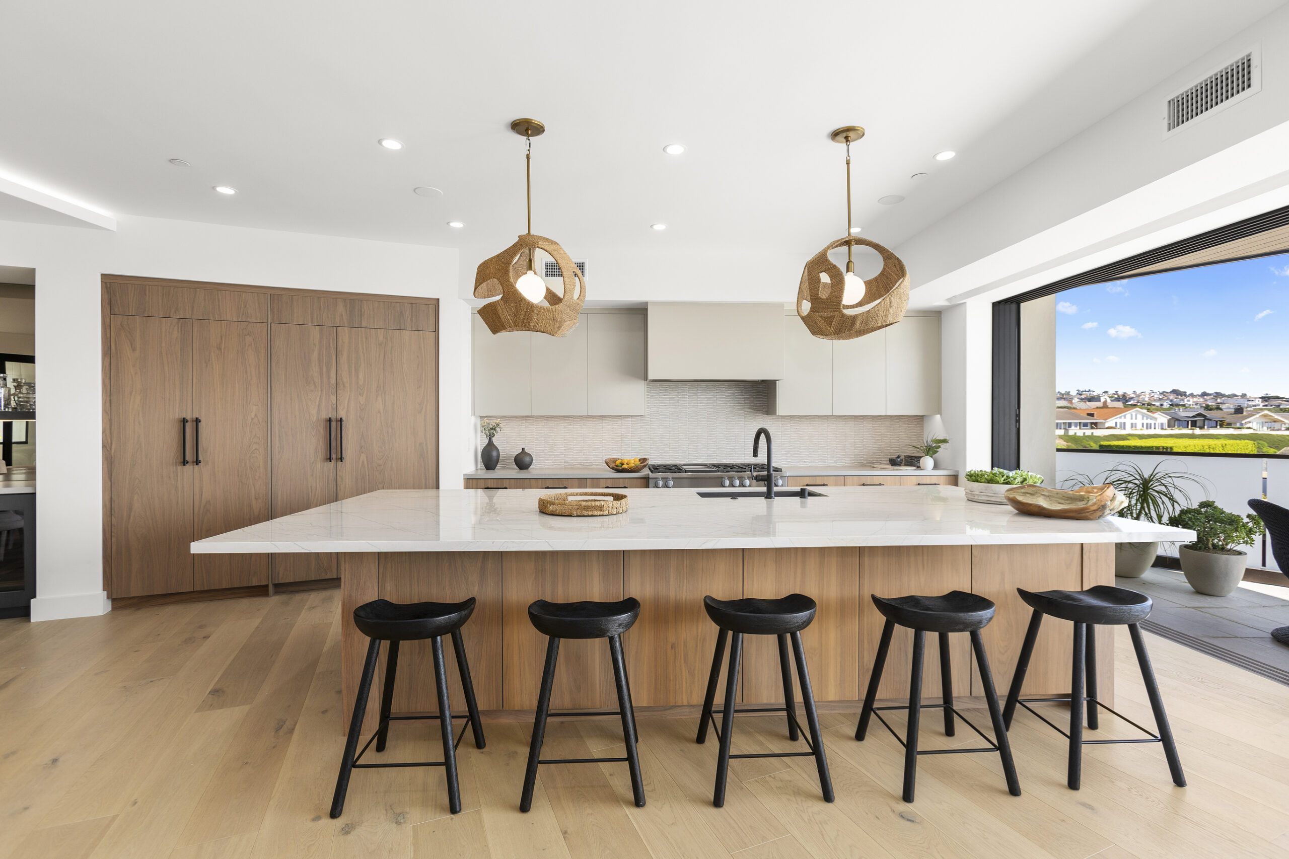 The chef’s kitchen is anchored by a large central island and appointed with a premium appliances, custom cabinetry, and a curated mix of quartz and quartzite countertops.