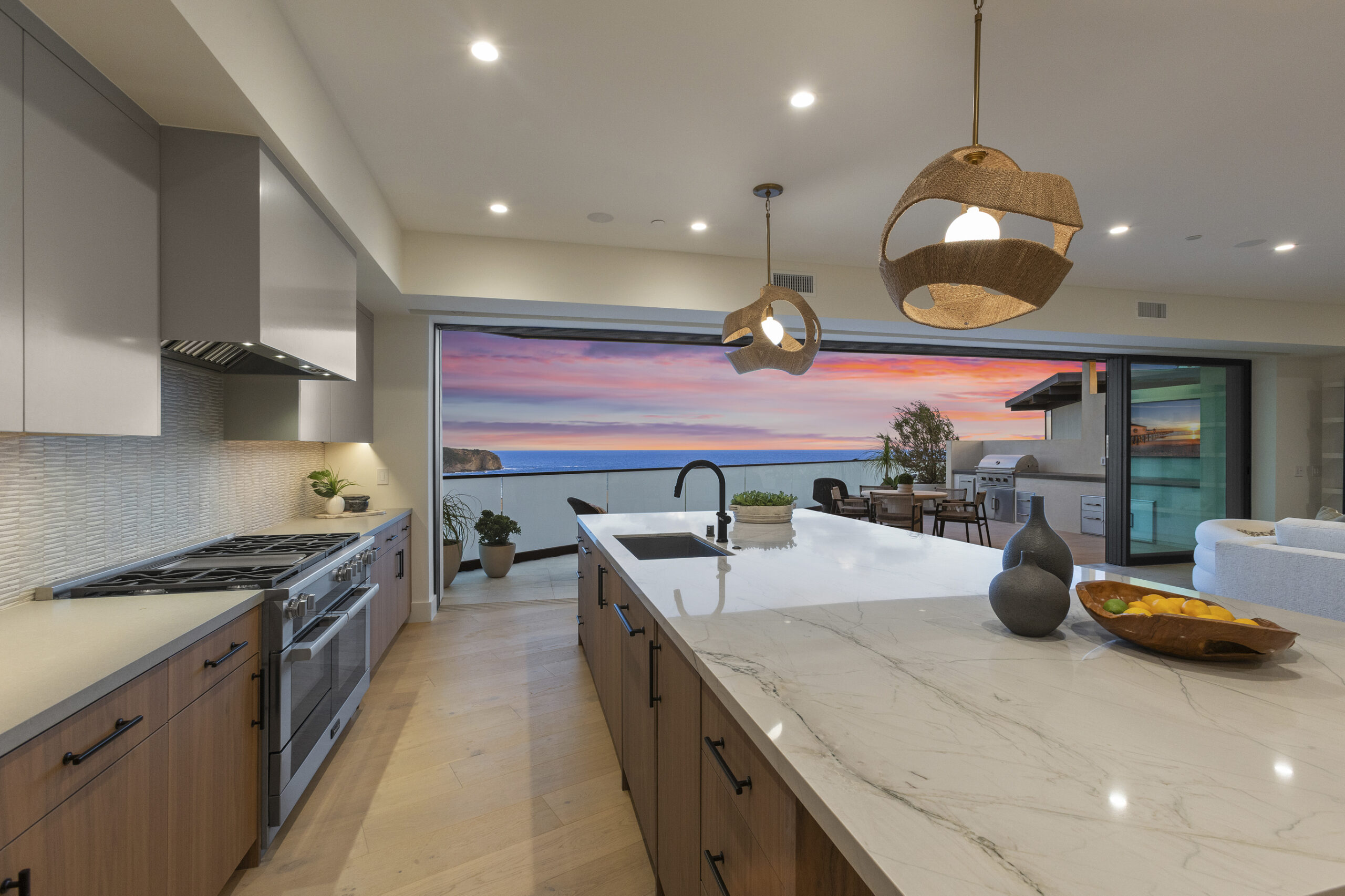 An open-concept kitchen that flows seamlessly to the outdoors through expansive sliding glass doors. The chef’s kitchen is anchored by a large central island and appointed with a premium appliance package, custom cabinetry, and a curated mix of quartz and quartzite countertops.