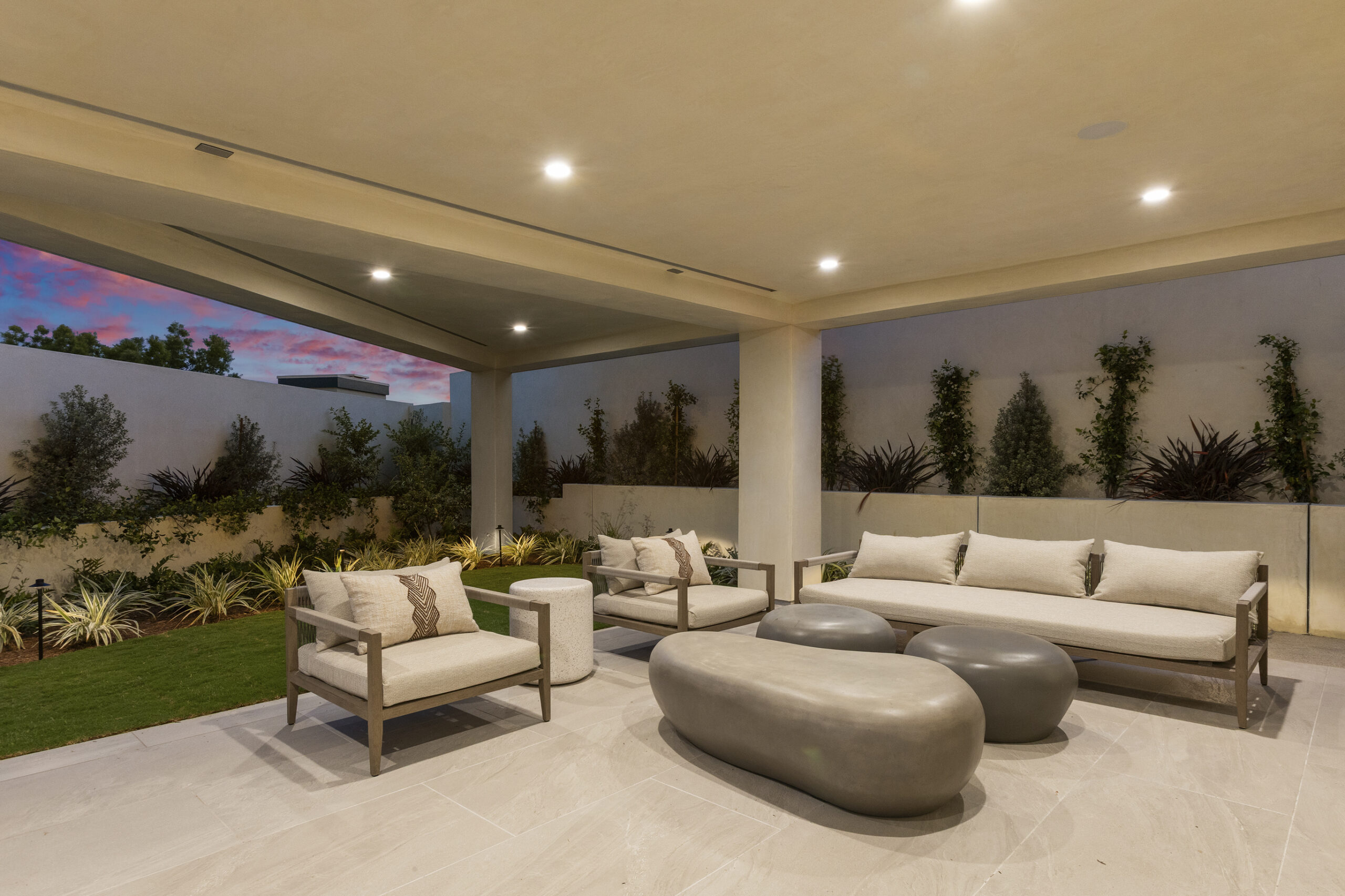 Thoughtfully composed landscaping on the lower deck softens the architecture while enhancing privacy and approach of this covered patio. Lounge area with comfortable couch and two chairs with modern oval coffee table provides the perfect space for outdoor living.